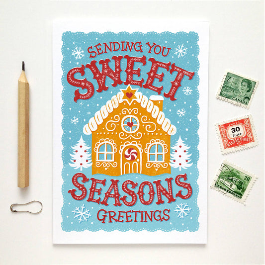 Christmas Cards. Blank inside. Gingerbread house on a turquoise background with snowflakes. Text is Sending you sweet seasons greetings.