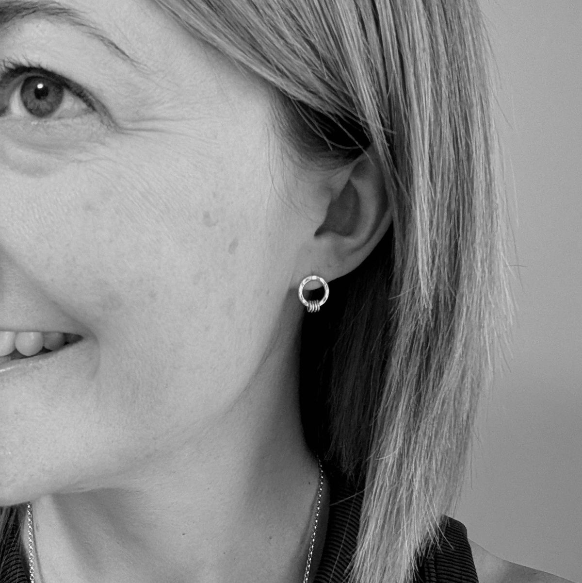 A close-up black and white photo of a woman's ear wearing a small silver hoop earring.