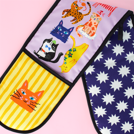 Two oven mitts with colorful cat designs on a pink background