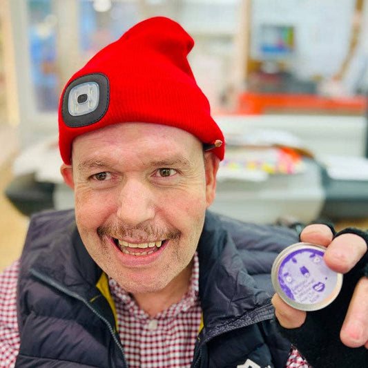 Man wearing a red beanie with a camera lens and holding a small round object.