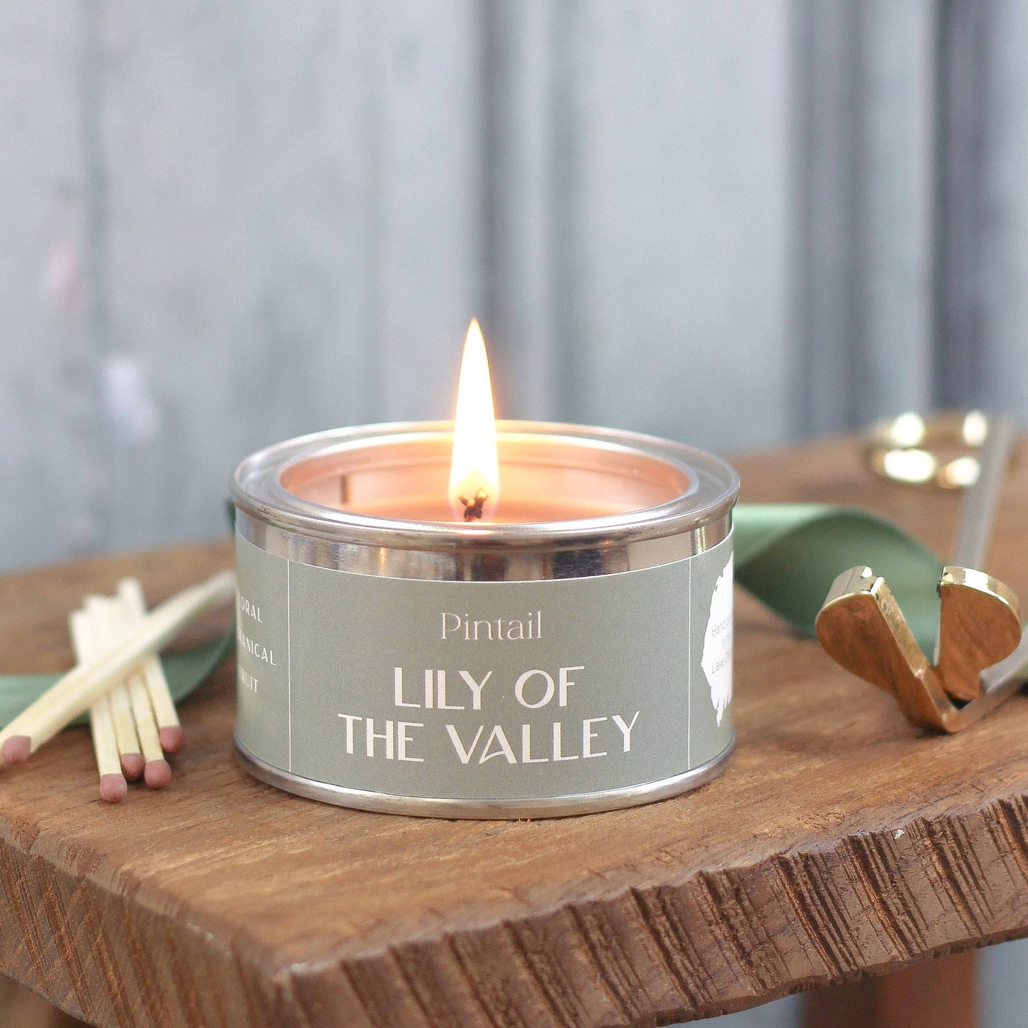 Candle labeled 'Lily of the Valley' by Pintail on a wooden surface with matches and a green container.