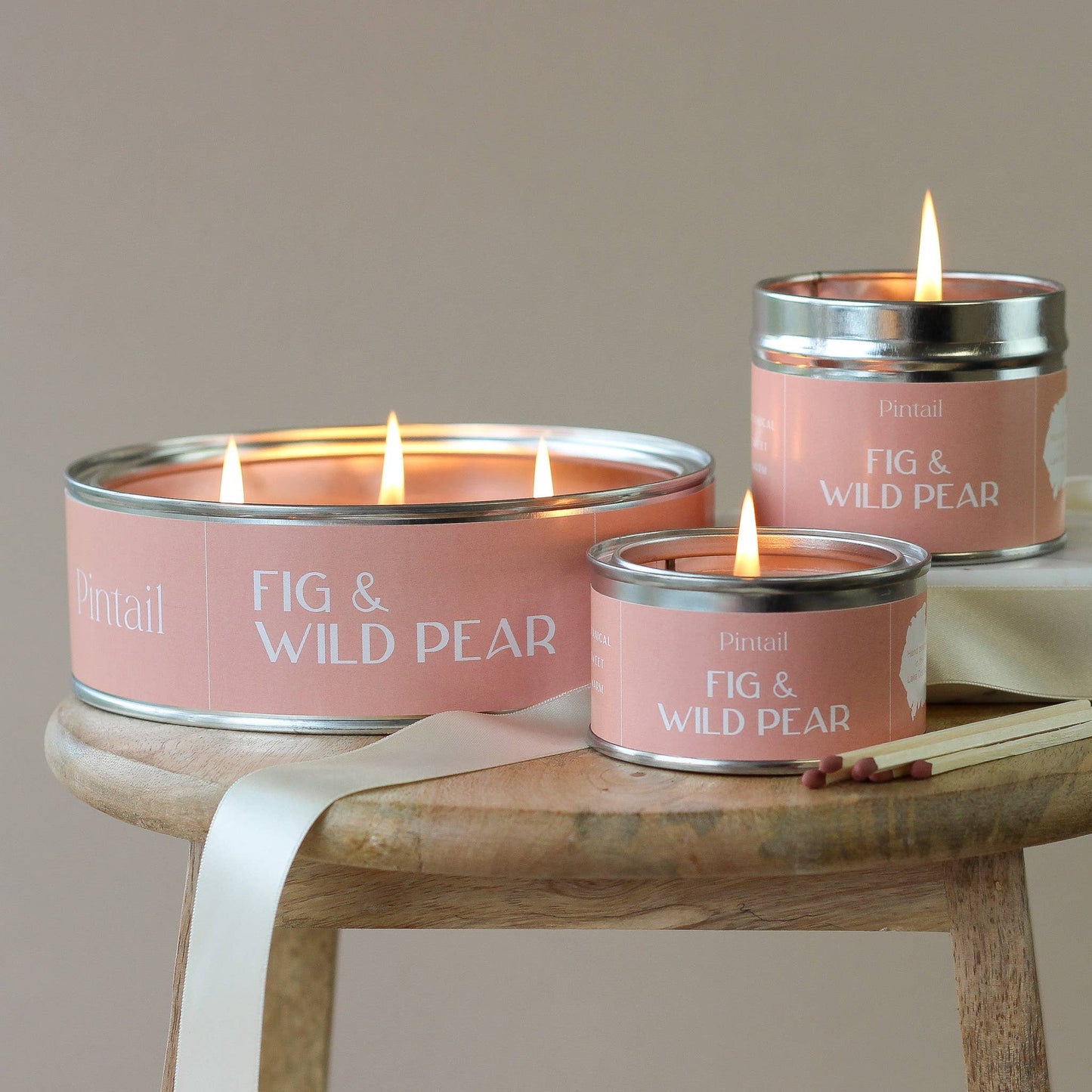 Three 'Fig & Wild Pear' candles on a wooden surface with a neutral background