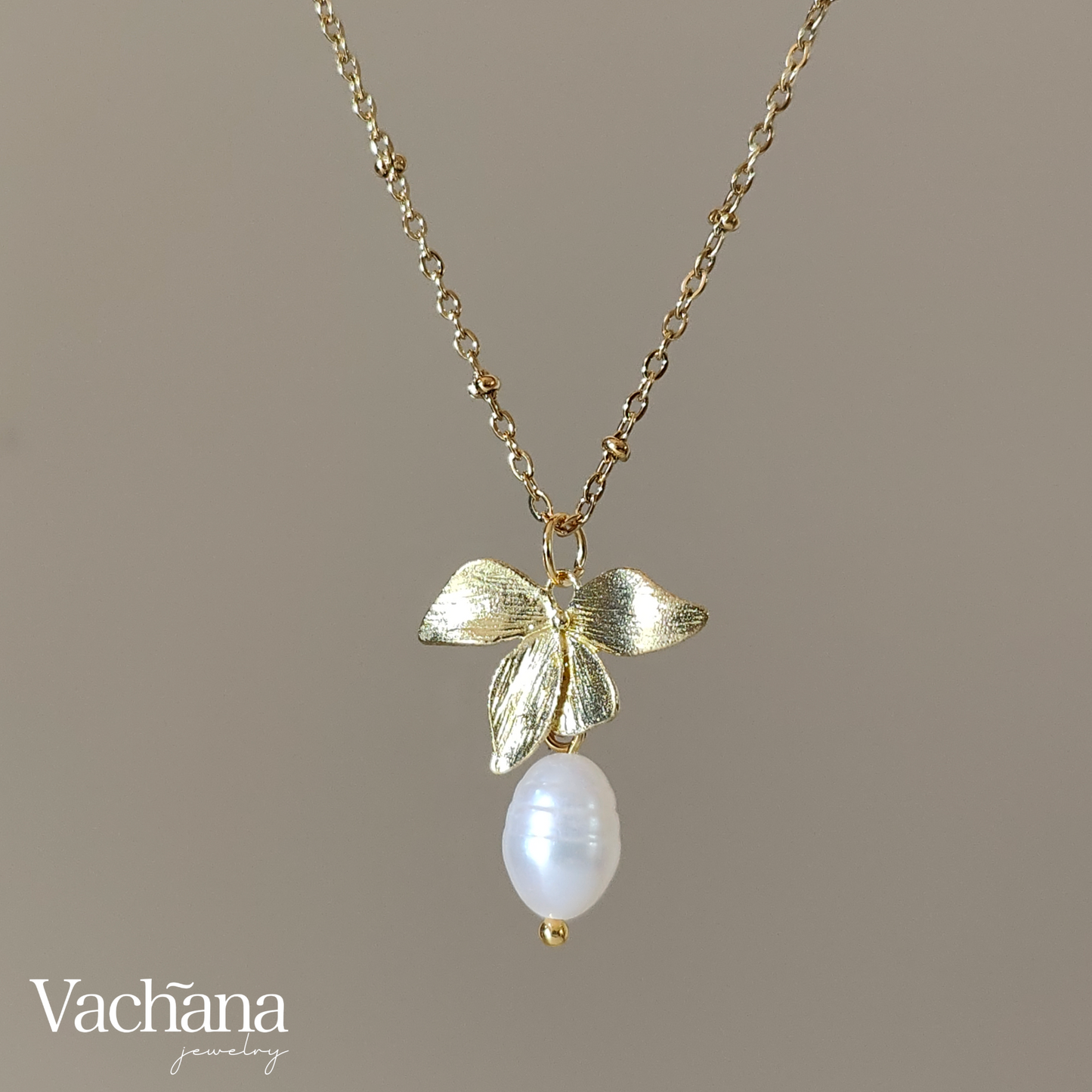 Gold necklace with leaf design and pearl pendant on a brown background, featuring the brand 'Vachana'.