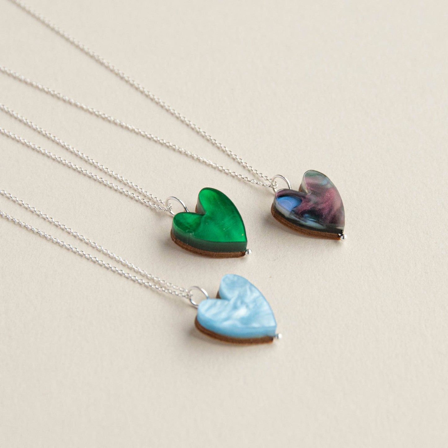 Three heart-shaped pendants on silver chains against a beige background