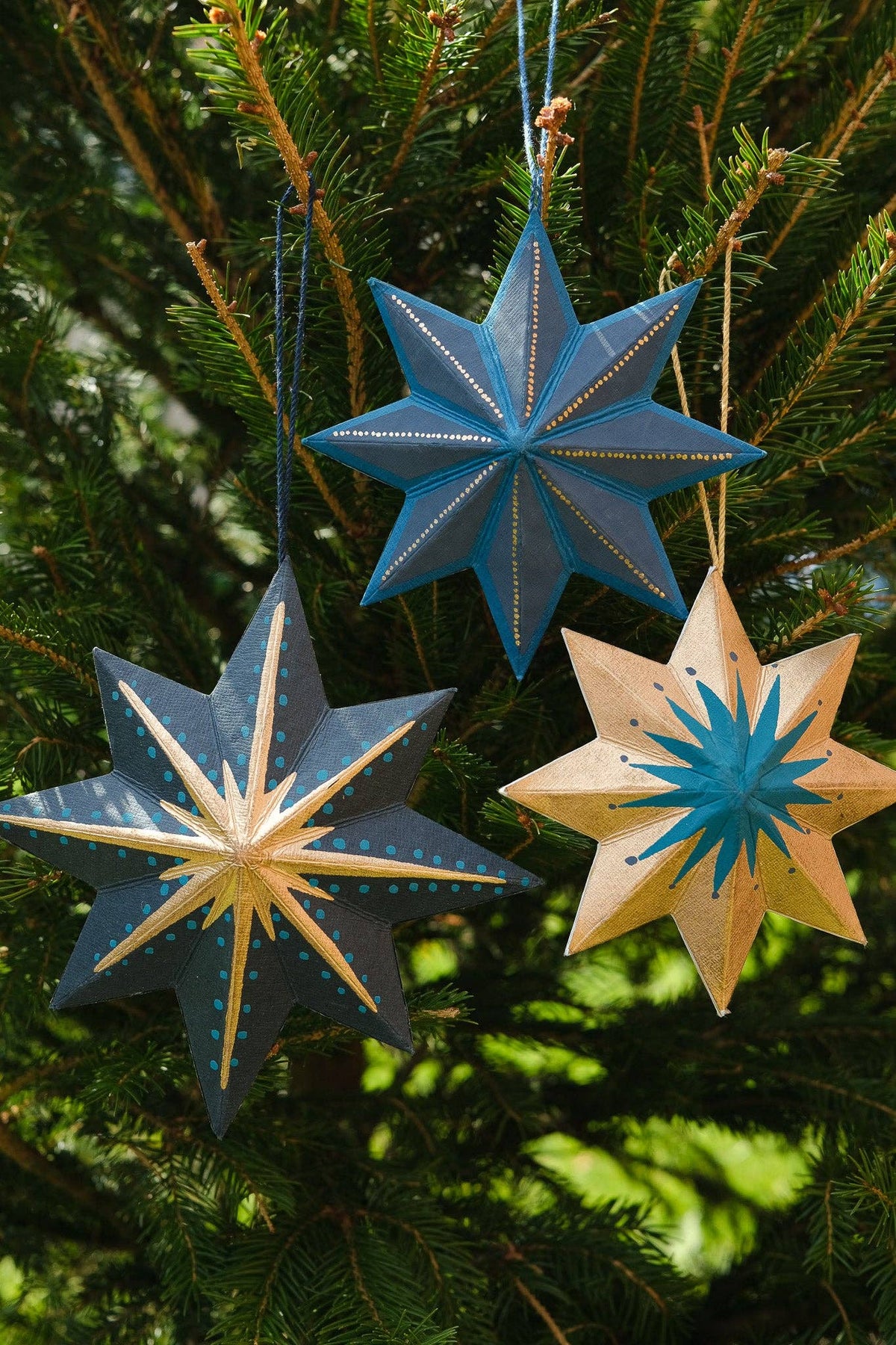 Three star-shaped Christmas ornaments hanging on a tree.