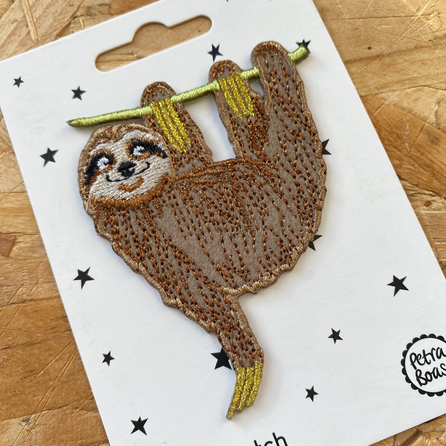 Embroidered patch of a sloth on a white card with star patterns, brand 'Petit Bear' visible.