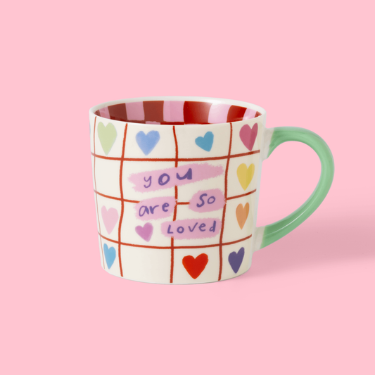 Mug with colorful heart design and 'you are so loved' text on a pink background
