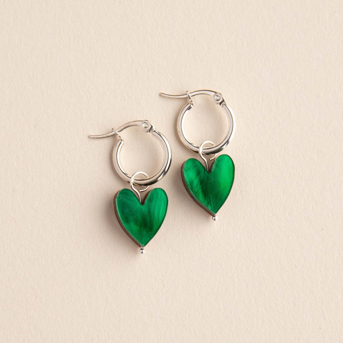 Silver hoop earrings with green heart charms on a beige background