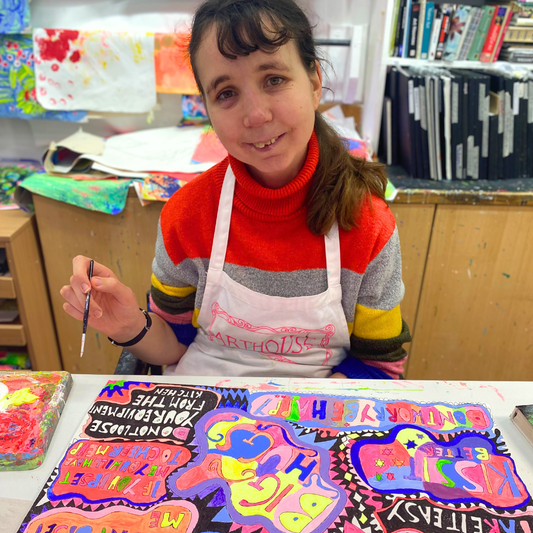 Person in a classroom setting with colorful artwork and art supplies.