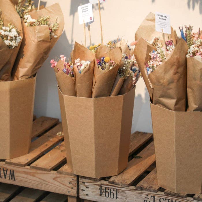 Bouquets of flowers in brown paper bags on a wooden pallet.