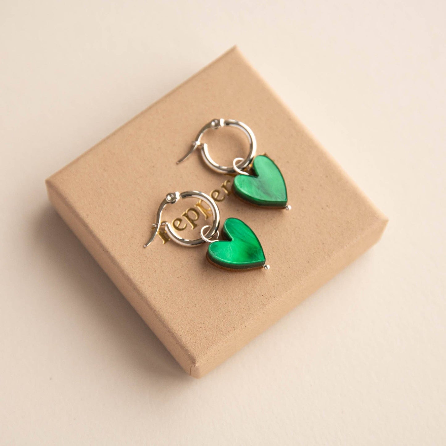 Green heart-shaped earrings on a beige box