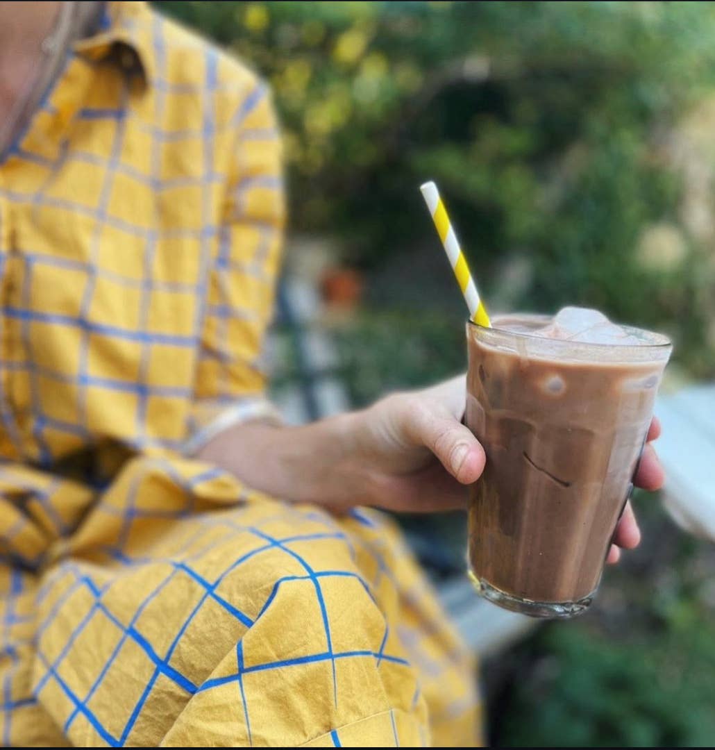 Person holding a glass of iced coffee with a straw outdoors