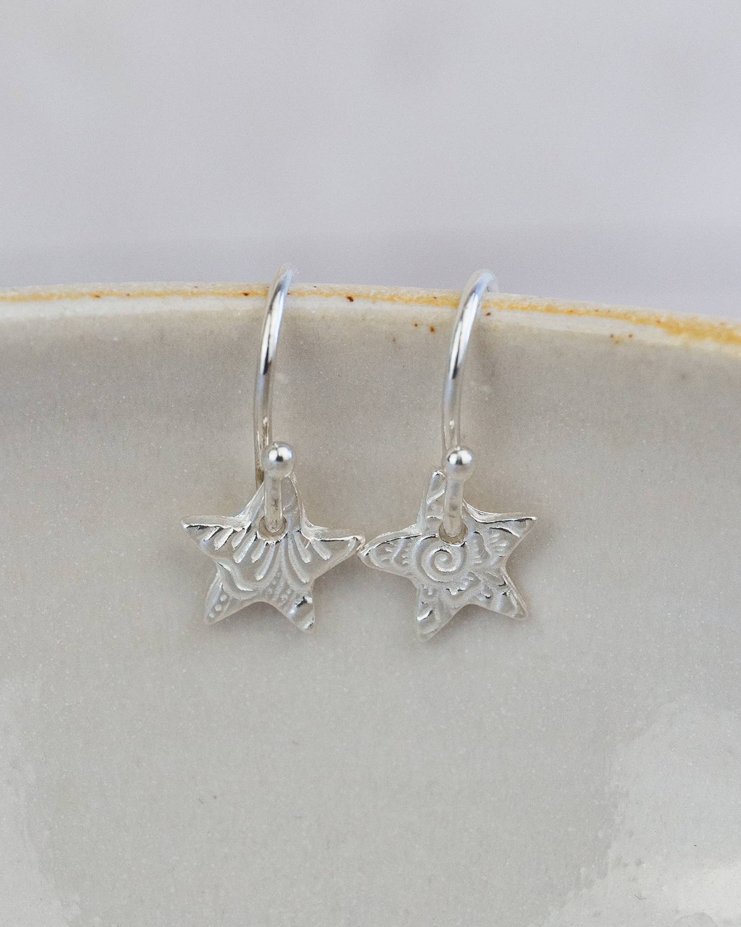 Silver star-shaped earrings on a white ceramic plate