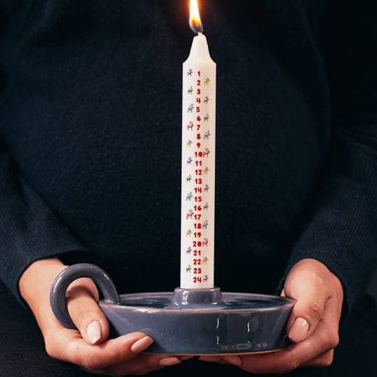 Candle with numbered days held in a dark container against a dark background