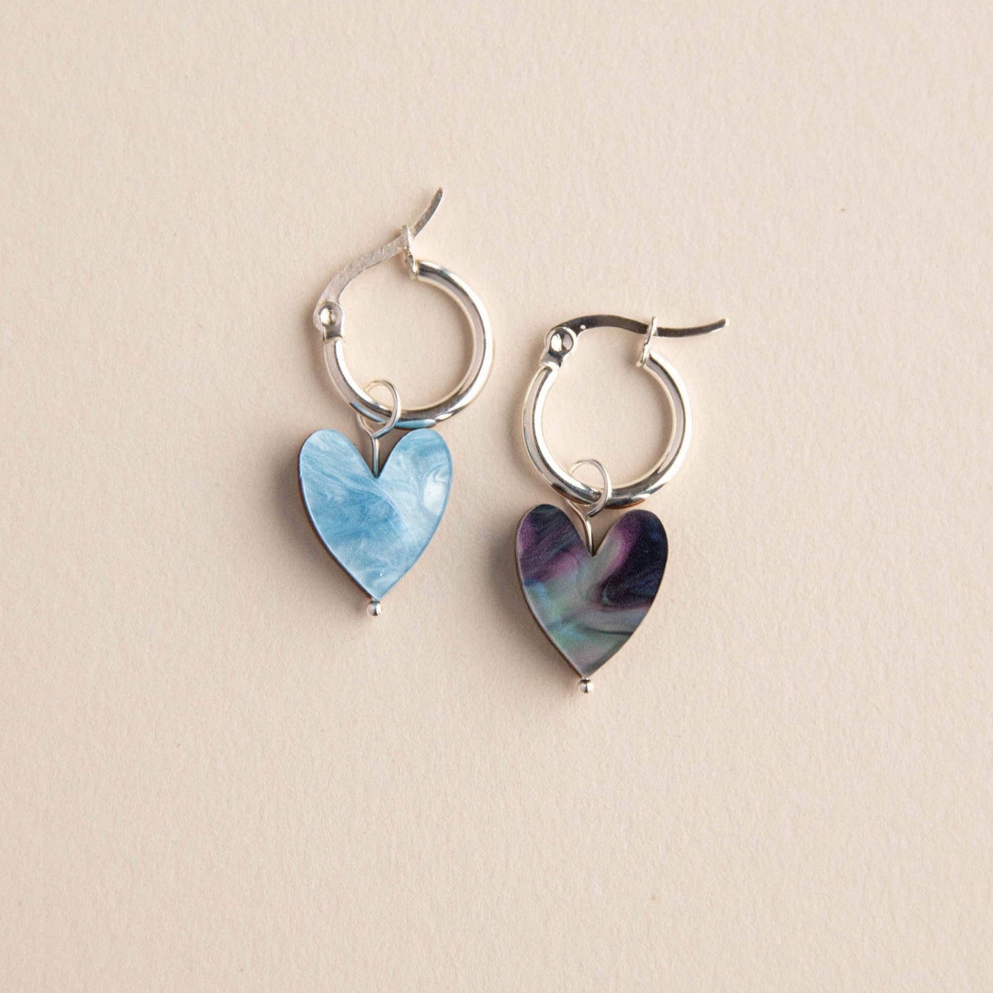 Pair of hoop earrings with heart-shaped charms on a beige background