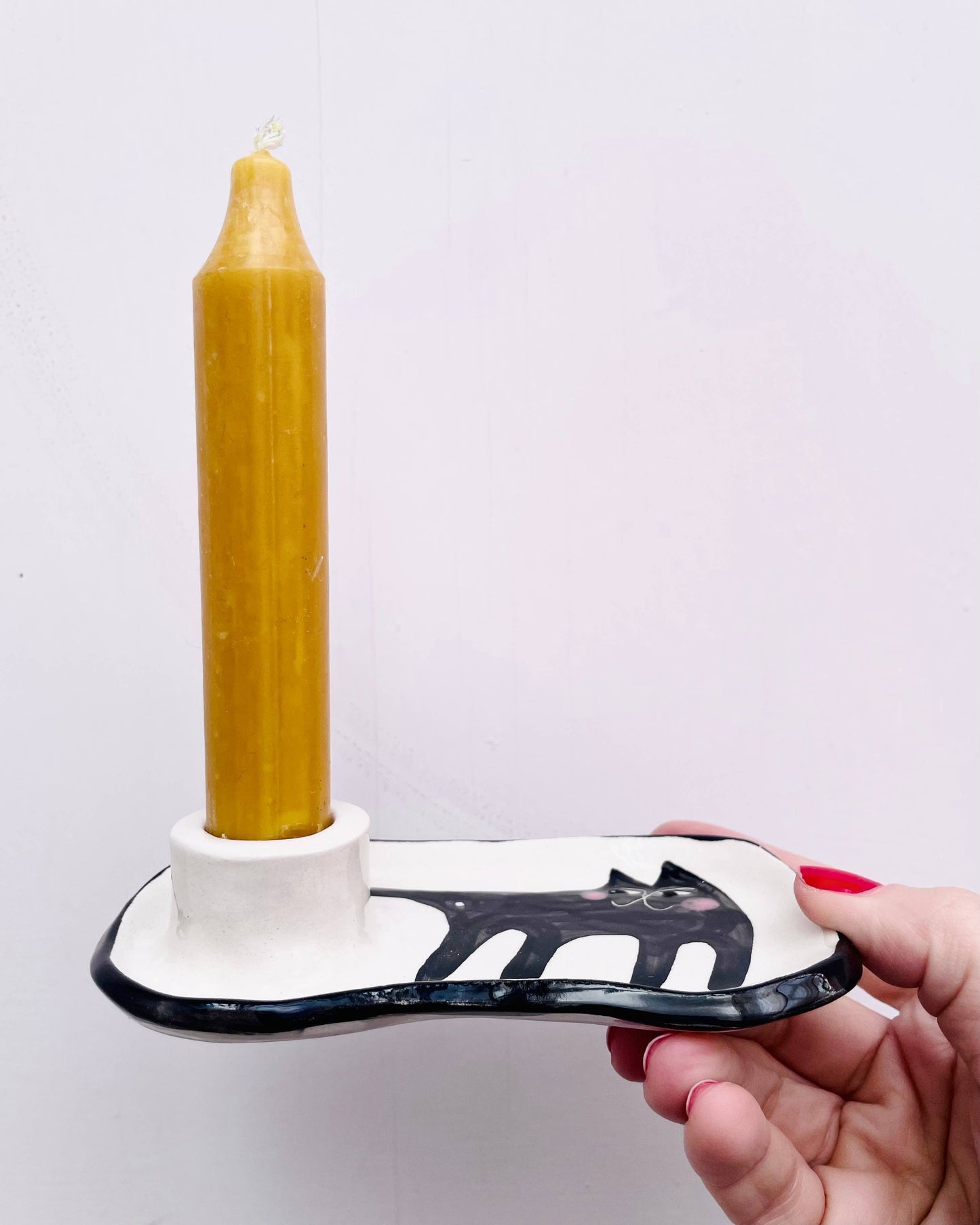Hand holding a white and black tool with a yellow candle on a white background