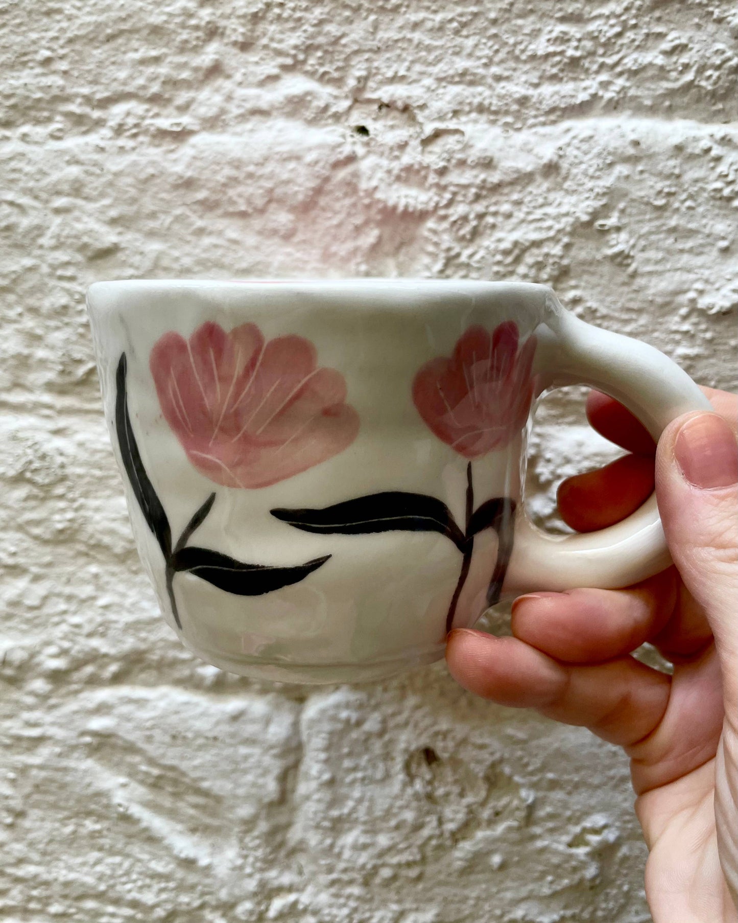 Hand holding a ceramic mug with floral design against a textured wall.