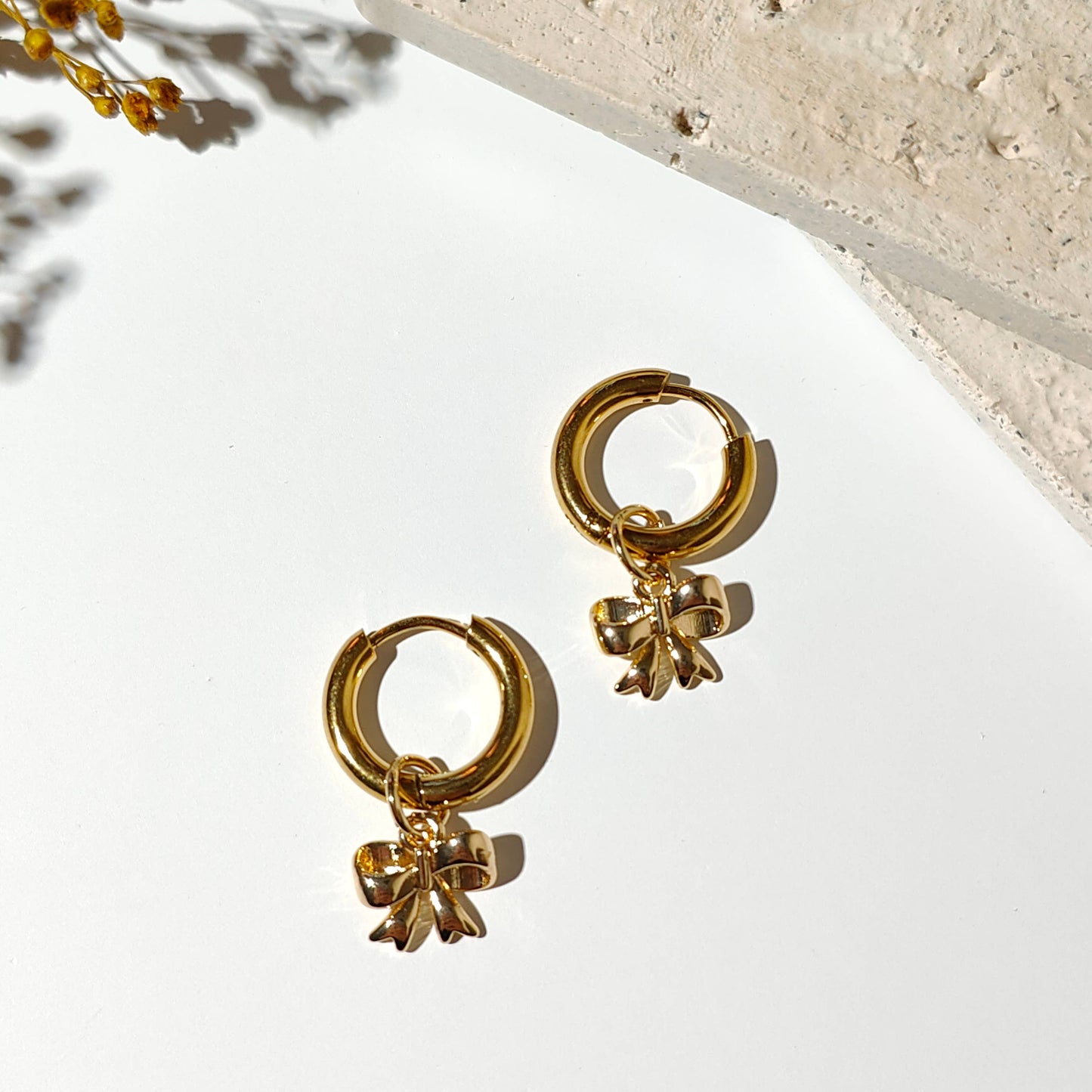 Gold plated hoop earrings with a bowtie ribbon charm