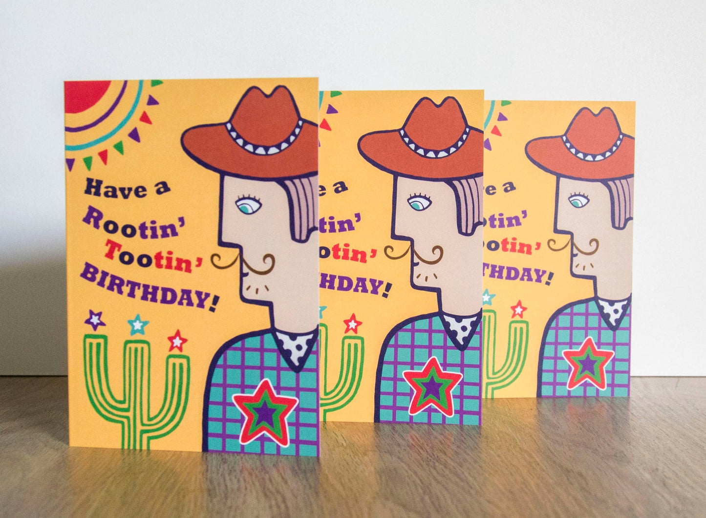 A card depicting a moustached cowboy next to a cactus, with a yellow background. To the left of the cowboy there is text that reads "Have a Rootin' Tooting' Birthday!"