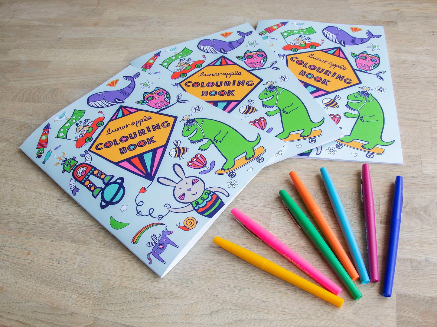 Three colouring books titled "Lunar Apple Colouring Book", surrounded by colourful drawings.
