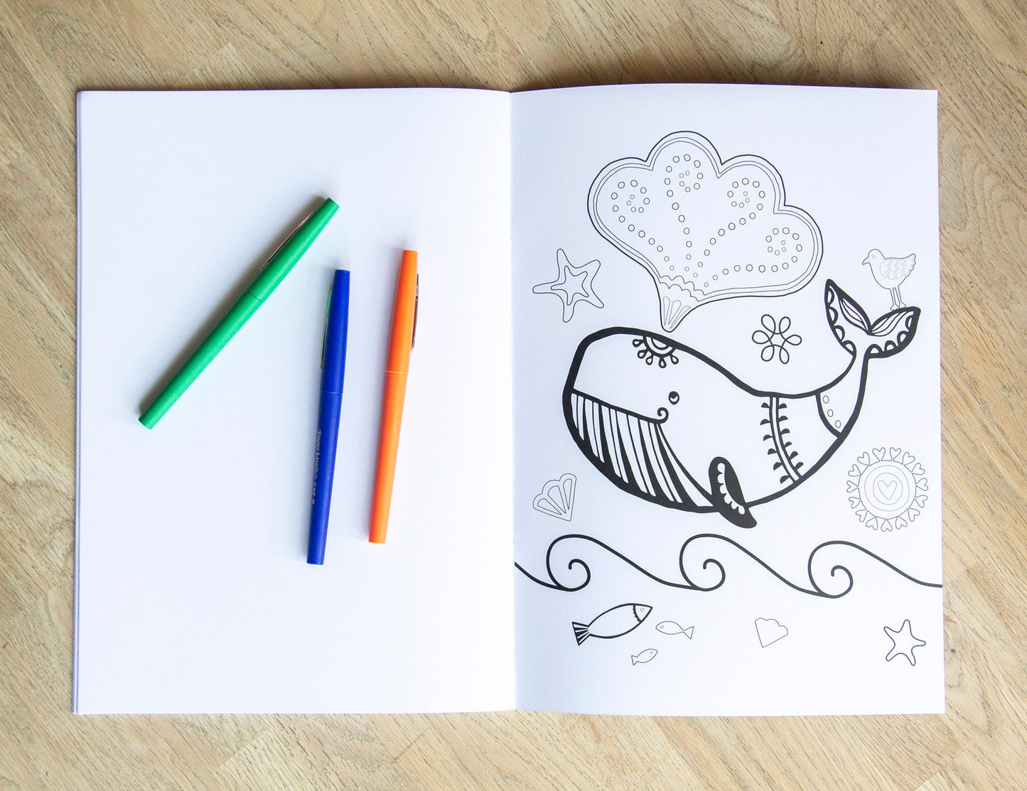 A colouring page book of a whale surrounded by fish and seashells.