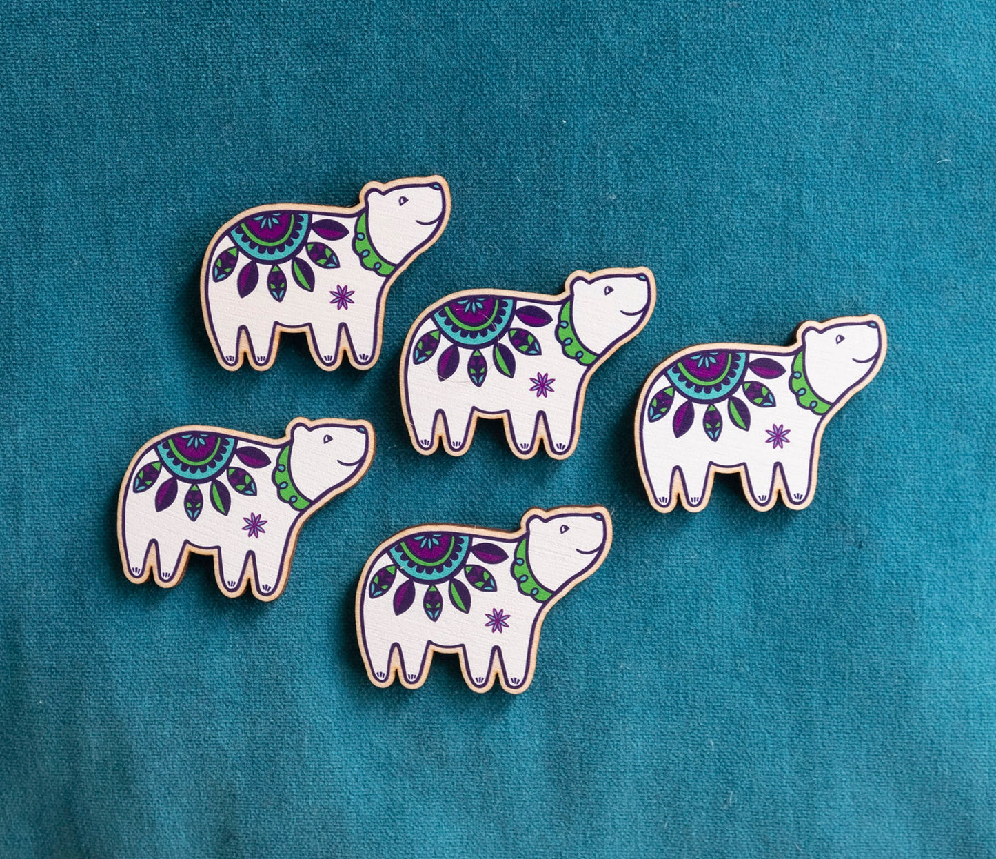 Five brightly painted wooden brooches of an art deco inspired smiling polar bear.
