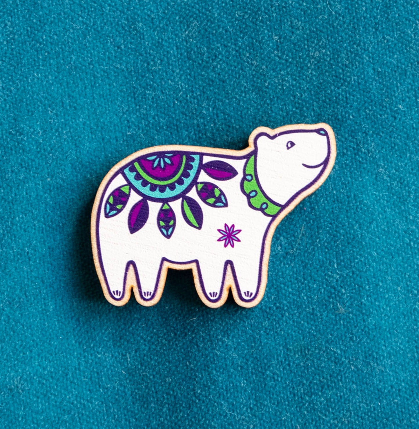 A brightly painted wooden brooch of an art deco inspired smiling polar bear.