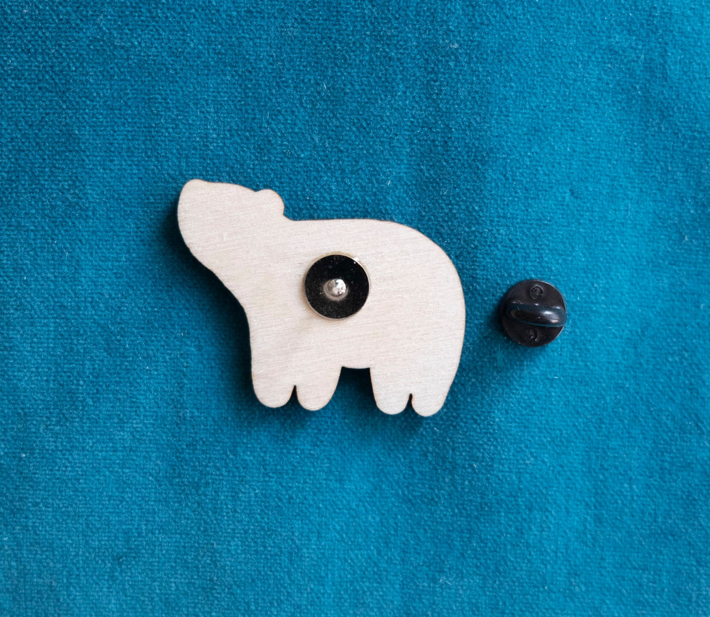 The back of a brightly painted wooden brooch of an art deco inspired smiling polar bear.