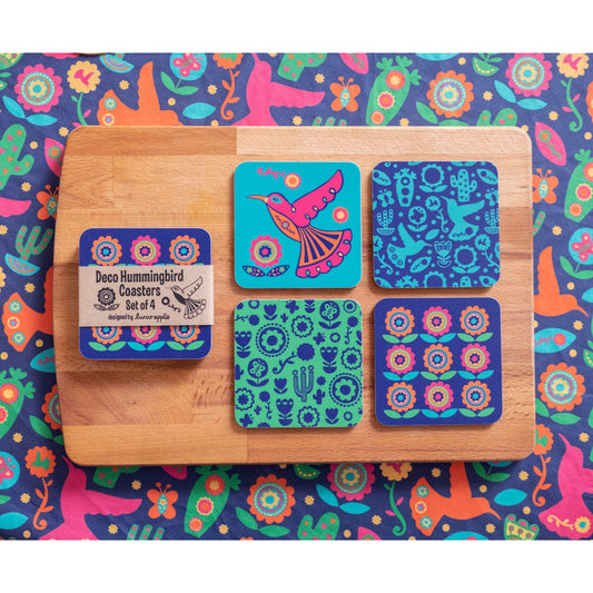 A set of four vibrant coasters featuring a hummingbird, hummingbird pattern, cactus pattern and flower pattern presented on a wooden board on top of a vibrant tablecloth.