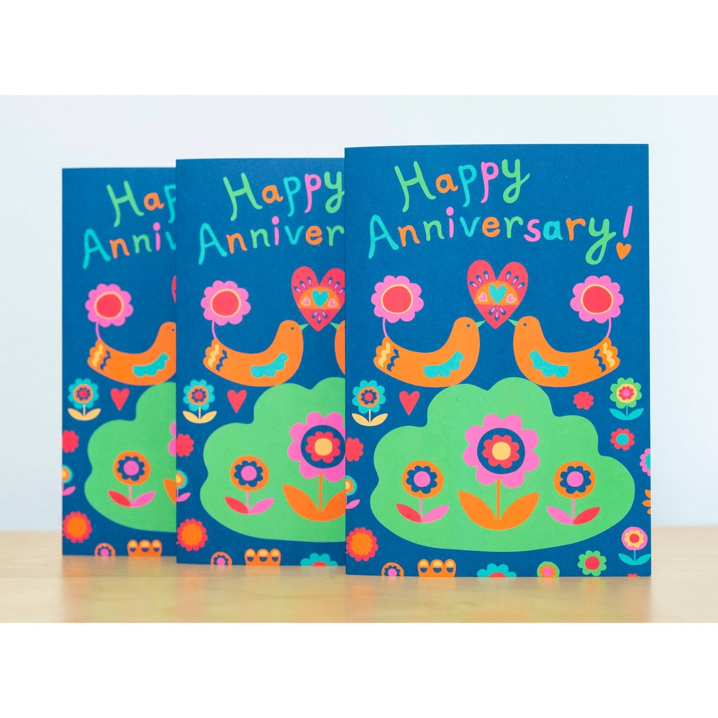 A card depicting two orange art deco birds holding up a heart together with their beaks. Above them reads the text "Happy Anniversary!"