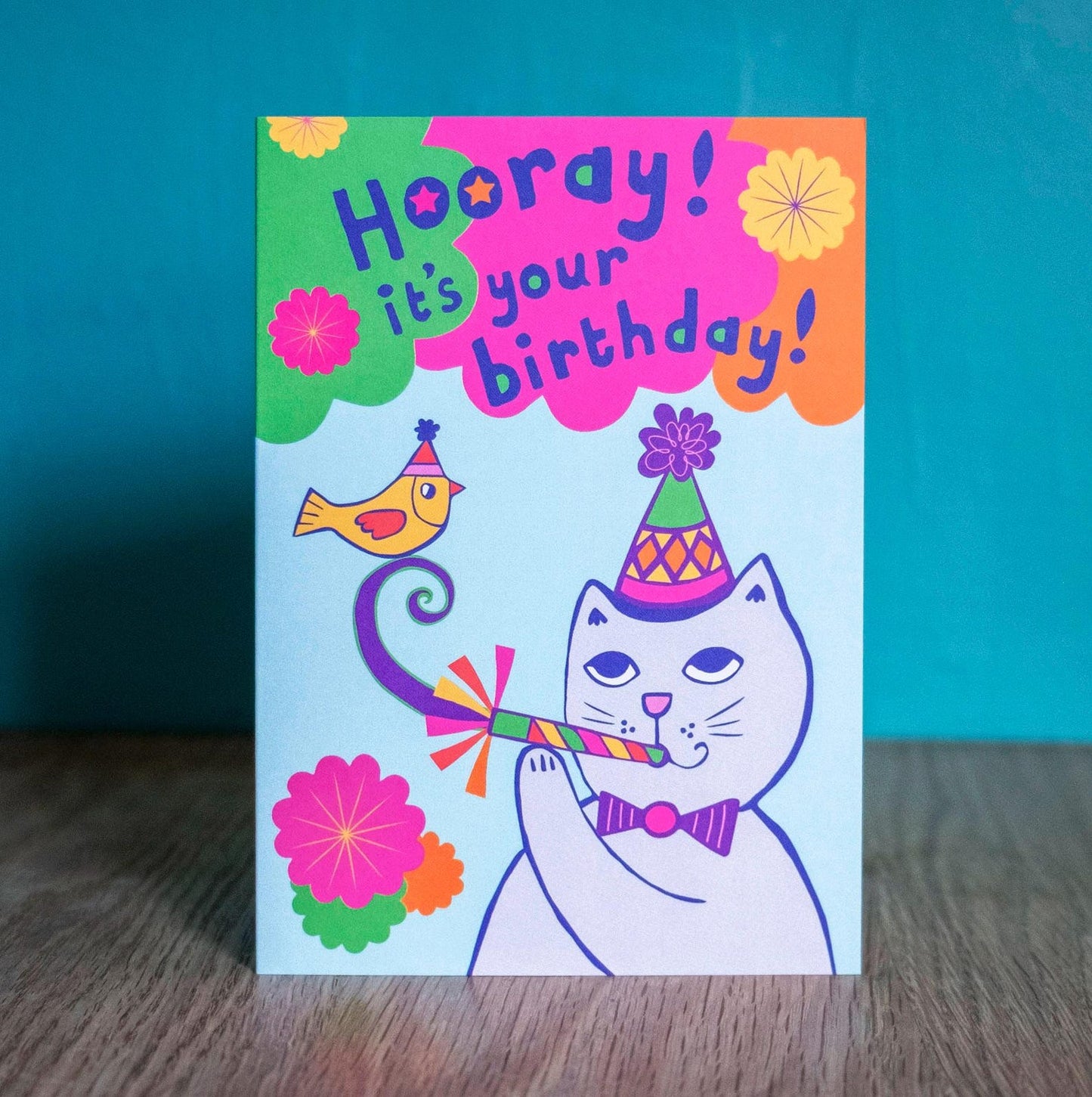 A card depicting a grey cat and yellow bird with party accessories, with the text "Hooray! It's your birthday!" above.