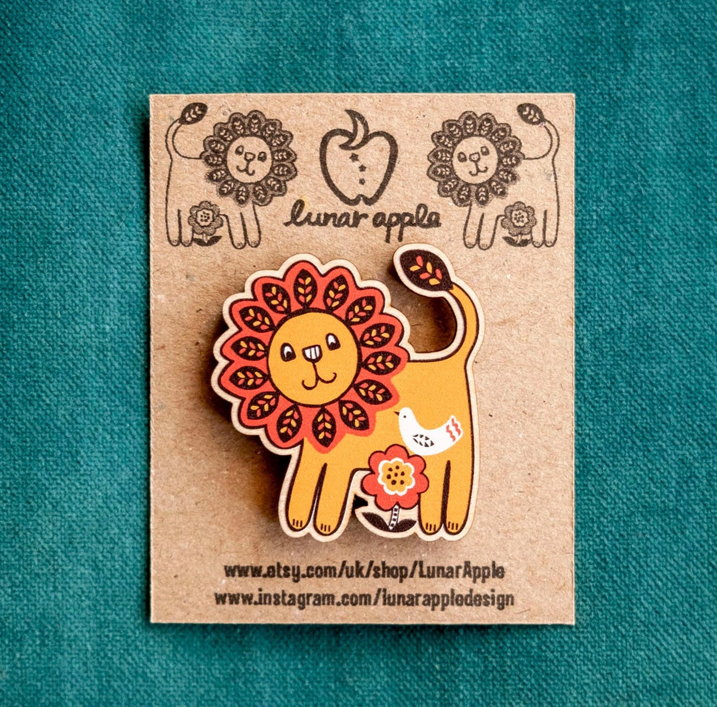 Lion-shaped pin on a cardboard backing with 'lunar apple' branding against a teal background