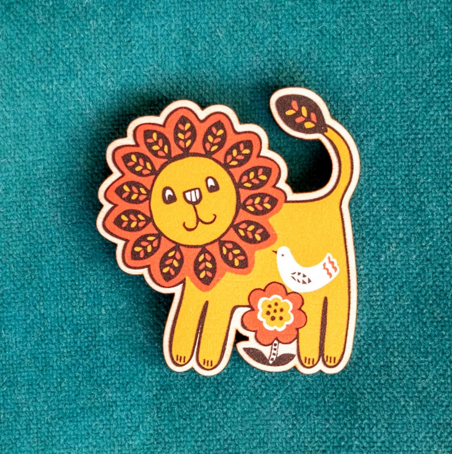 Colorful lion-shaped wooden pin with a smiling face against a teal background