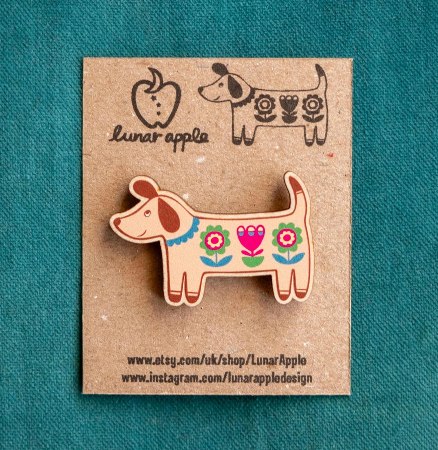 Colorful dog-shaped pin on a brown card with 'lunar apple' branding against a teal background