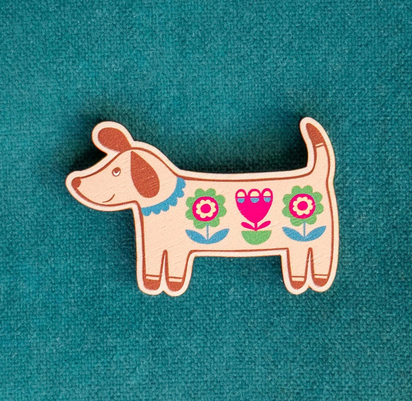 Decorative dog-shaped wooden brooch with floral patterns against a teal background