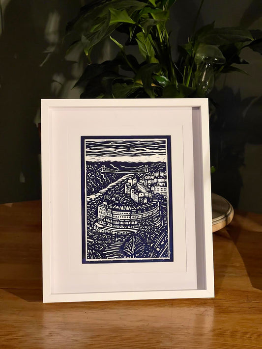 Framed artwork of a blue and white landscape on a wooden surface with a plant in the background.