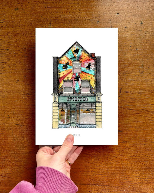 Hand holding a card with a colorful illustration of a building on a wooden surface