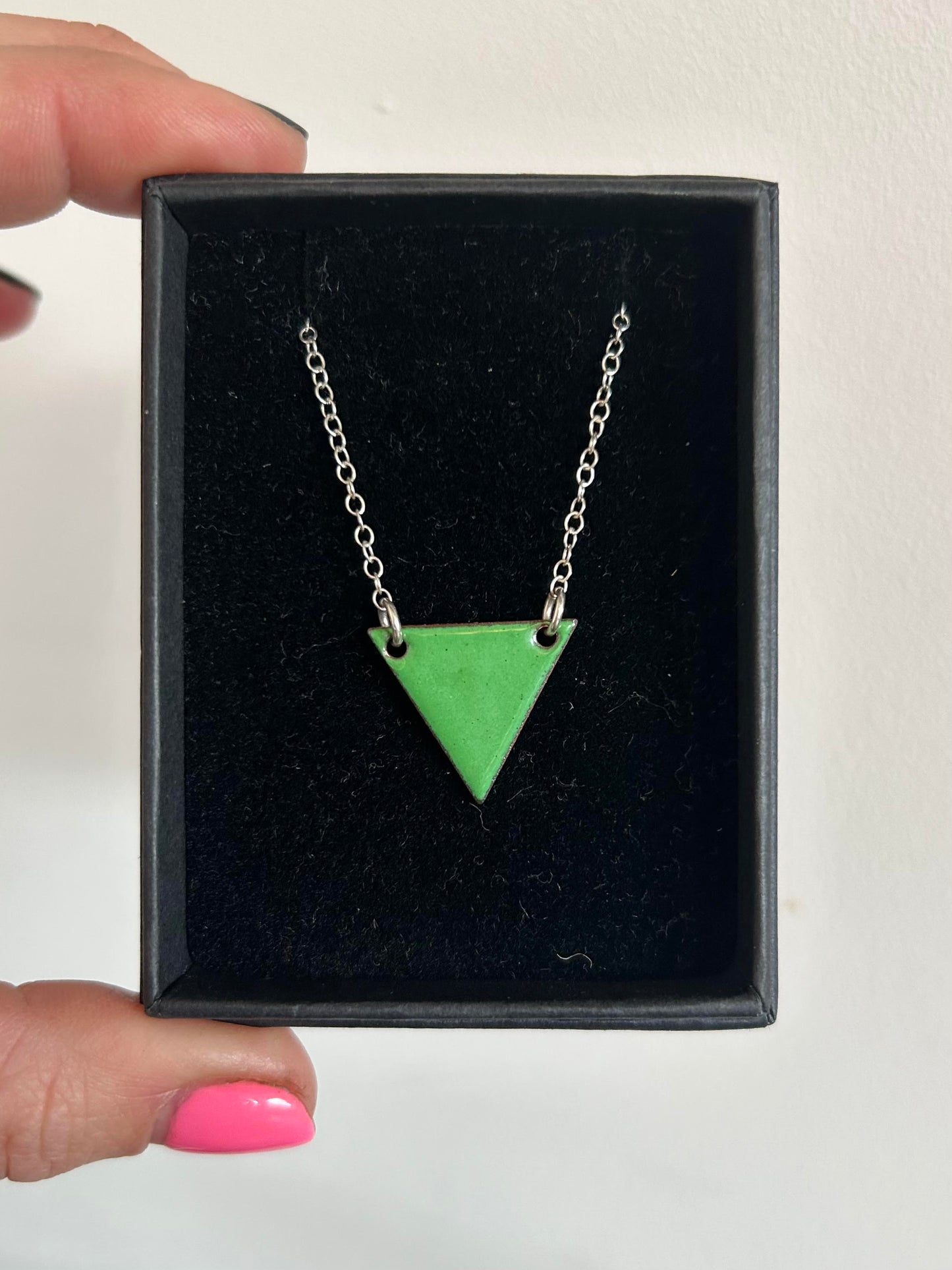 A green enamel triangle pendant with a silver chain in a box.