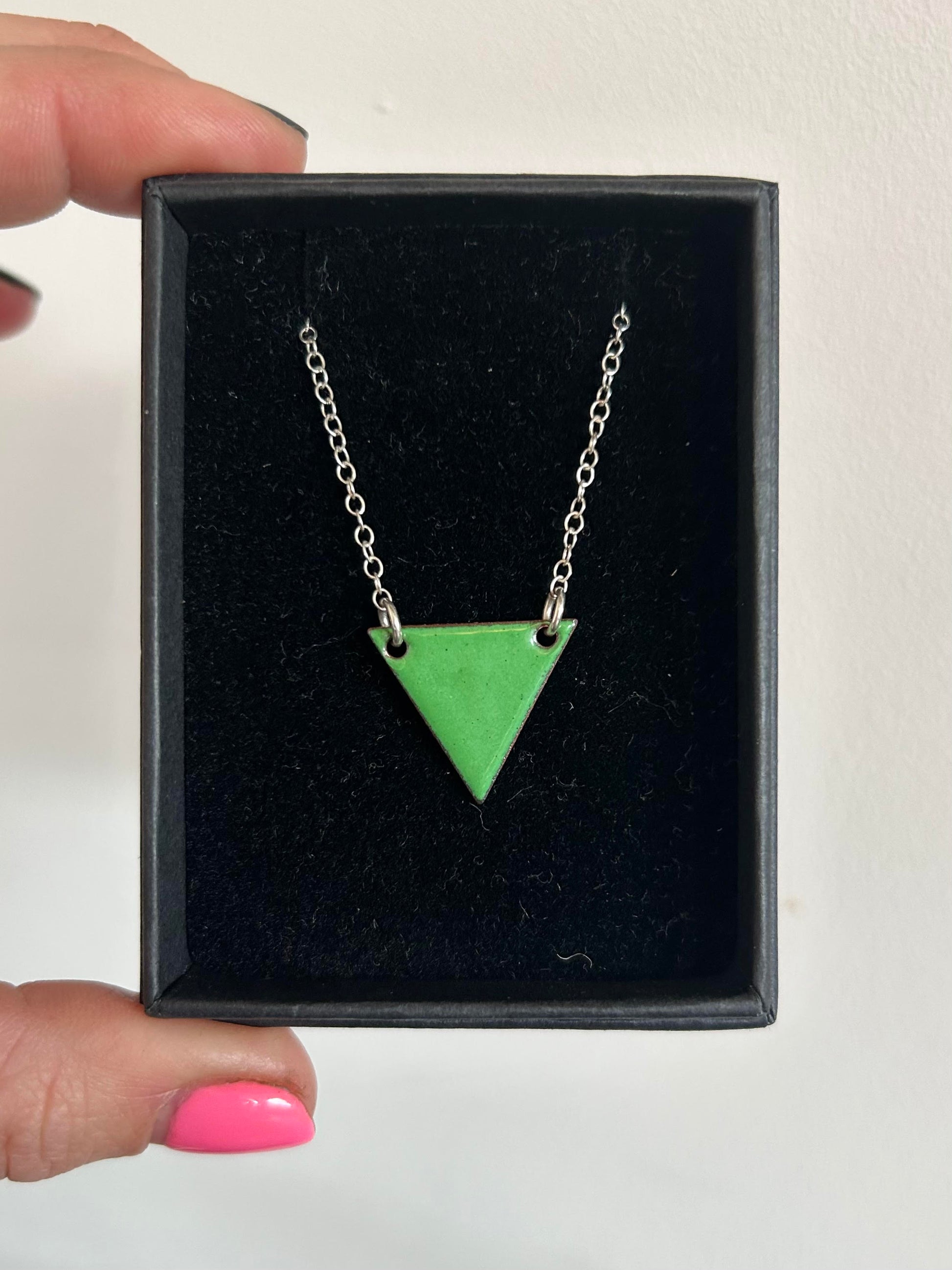 A green enamel triangle pendant with a silver chain in a box.