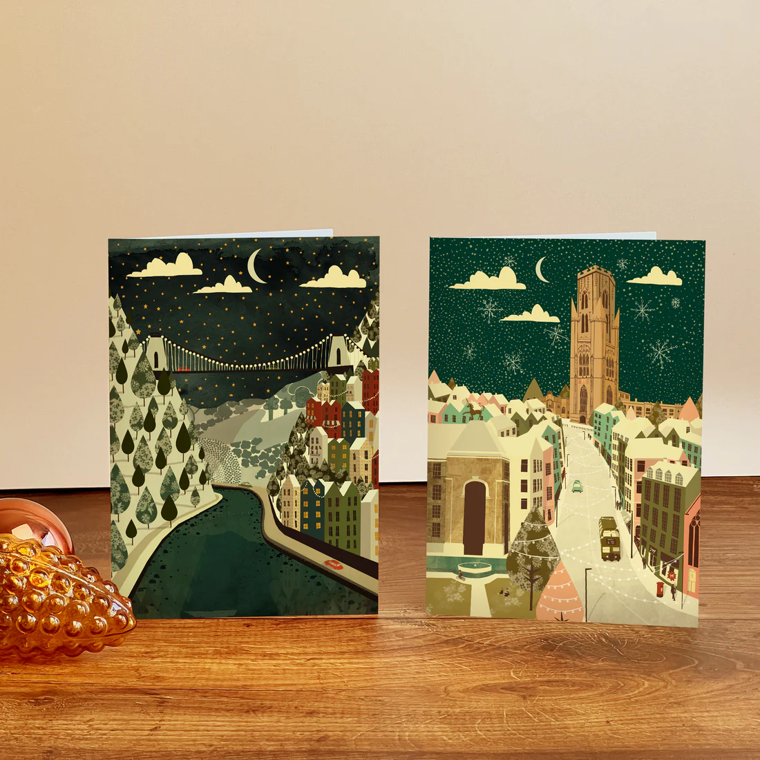 Two greeting cards with cityscape designs on a wooden surface.