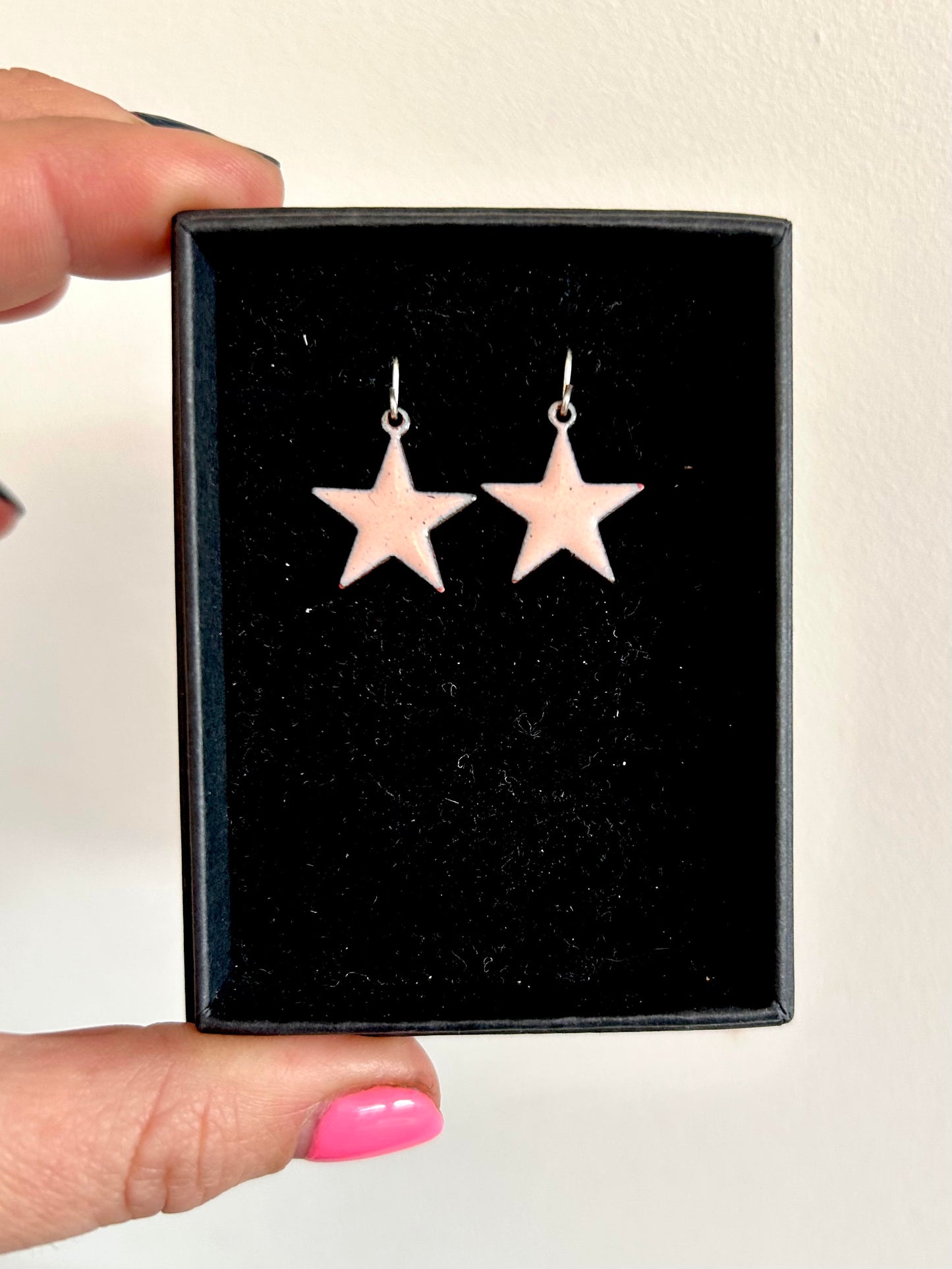 A pair of pale pink enamel star earrings in a box.