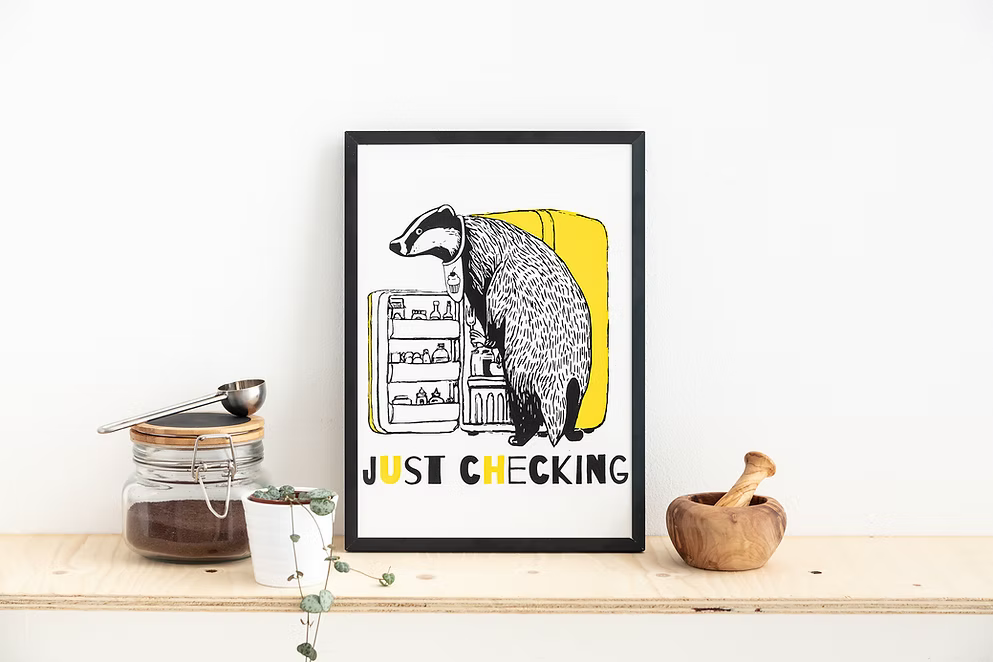 Framed artwork of a badger with 'Just Checking' text on a shelf.