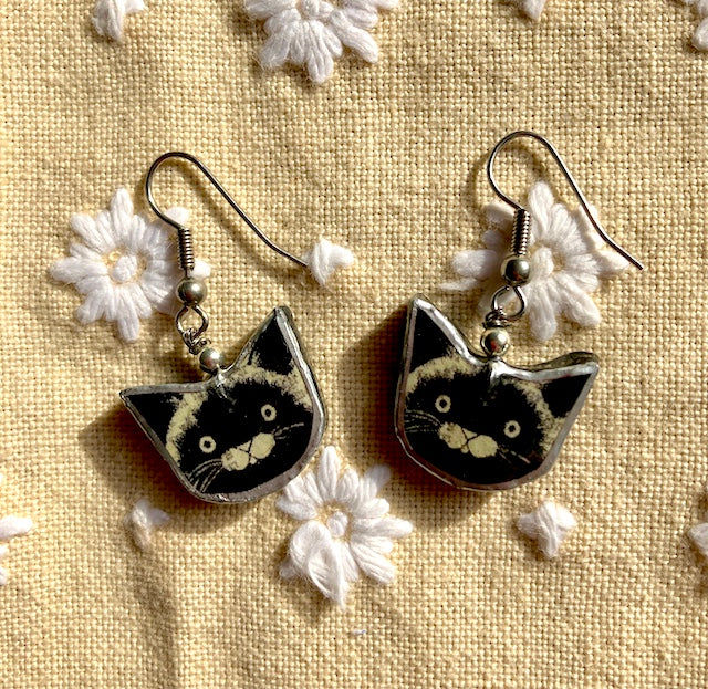 Layered paper, metal and resin used to create these happy black cat face earrings. Handmade in Cardiff, Surgical steel (hypoallergenic) earwigs.
