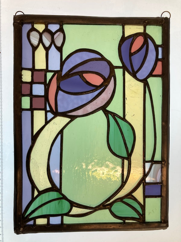 A Charles Rennie Mackintosh inspired stained glass hanging, with roses and leaves over a geometric design. Handmade by Dadswell Glass at Glass Designs in Bristol.