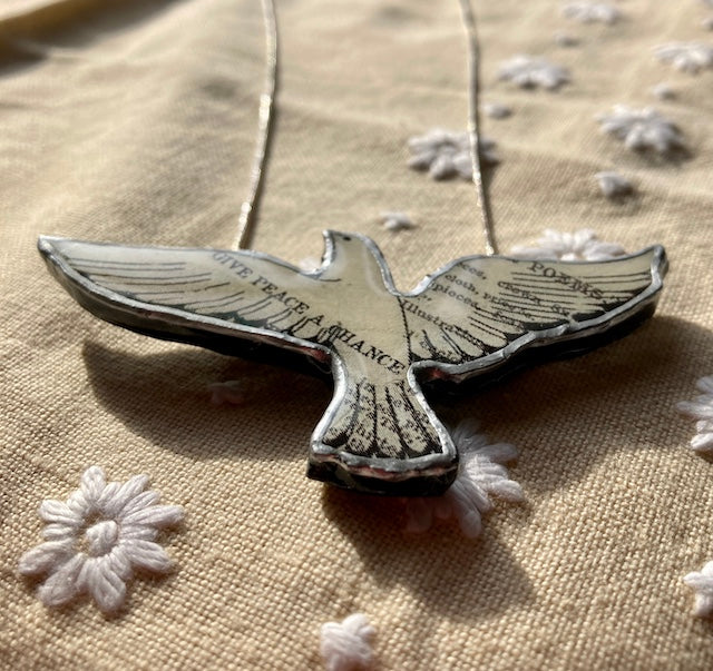 A dove on a 18 inch chain, dove made from layered paper and steel then heavily laquered in resin. The text Give Peace a Chance across one wing. Edit alt text