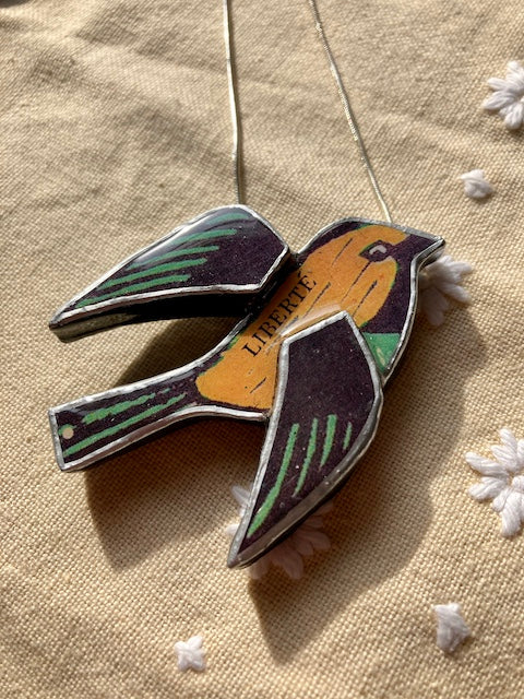 Handmade Pendant by Elymental a Cardiff based artist. Layered papers and metal and finished off with layers or resin. The chain is 18 inch silver plated. The text across the flying birds body ready Liberte Edit alt text