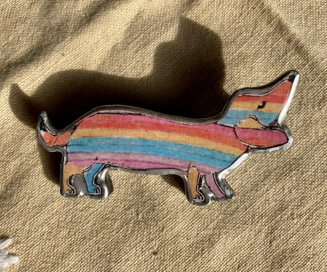 quirky rainbow striped sausage dog brooch, made from layered paper, metal and resin. Handmade in Cardiff by Ellymental.