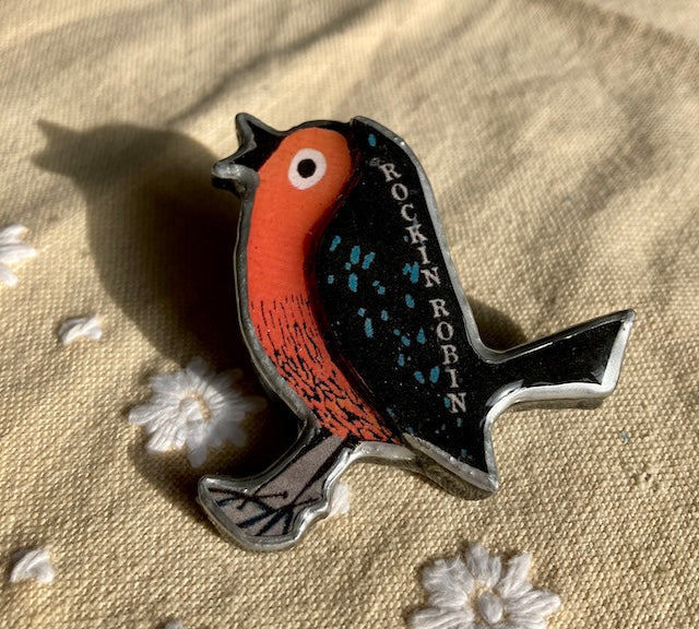 Layered paper, steel and resin creates this whimsical Robin Brooch. Handmade in Cardiff. Rockin Robin text on Robins wing.