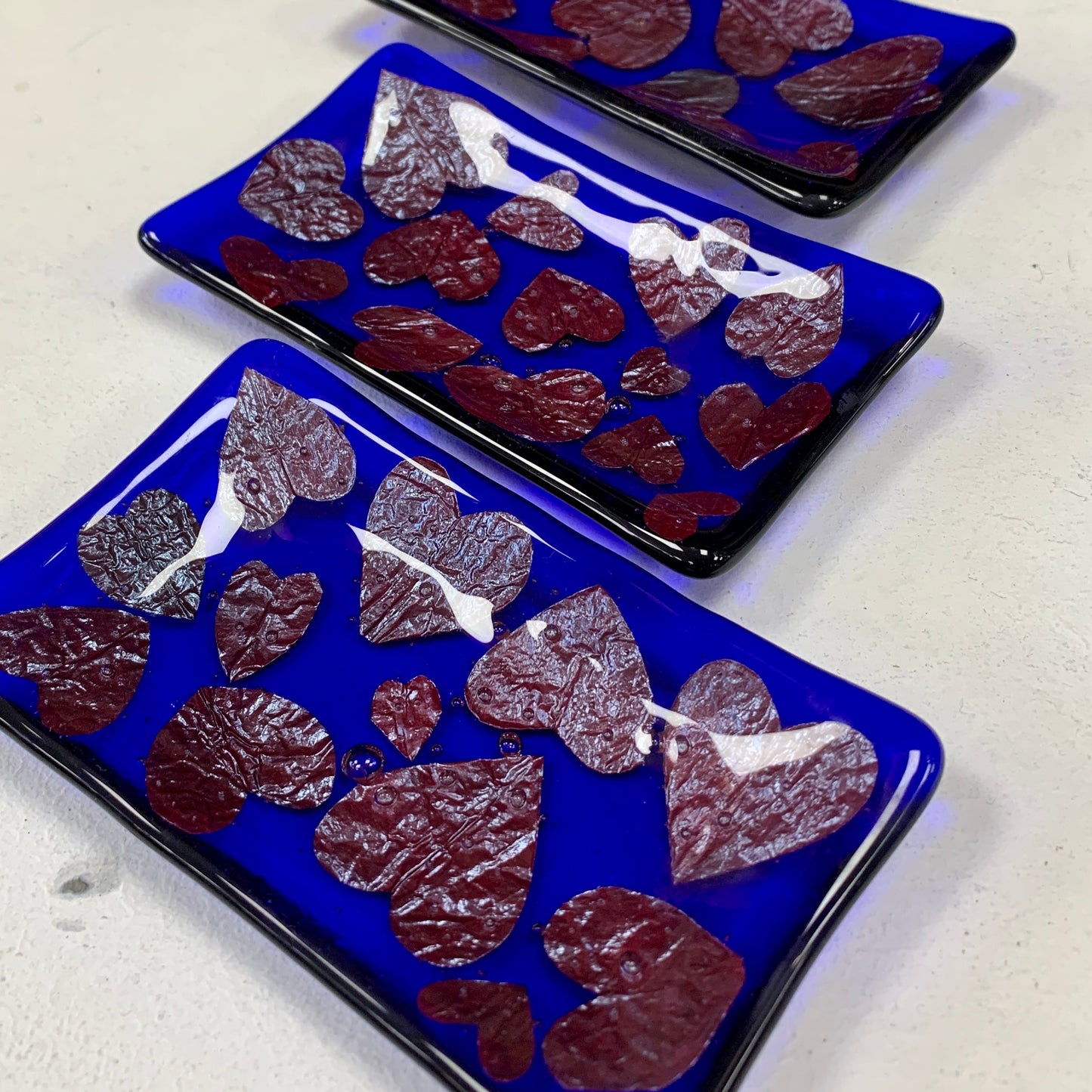 Bristol Blue Glass fused trinket dish or soap dish with Rusty red hearts fused between the glass. Handmade in Bristol.