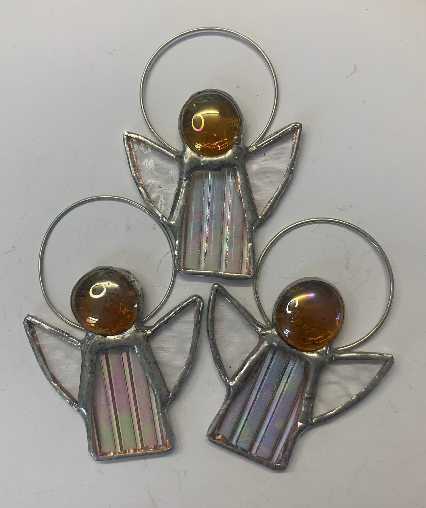 Stained Glass Angels. Individually made by hand. Many colour choices and variations. A choice of a clear or amber nugget head. The glass texture may vary slightly from the photographs. The clear glass wings will vary in texture too. Size 5cm x 7cm including halo. Glass is cut to shape and copperfoiled, followed by soldering all the pieces together. Handmade by Dadswell Glass at Glass Designs in Bristol.